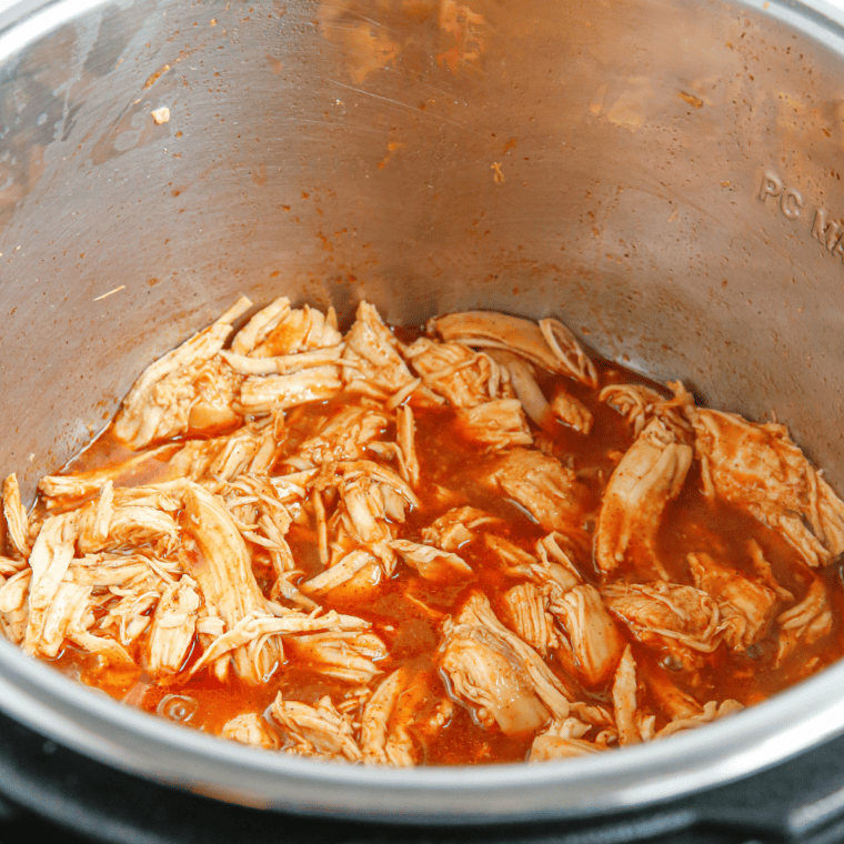 Shredded chicken stirred together with enchilada sauce and shredded cheese in a bowl