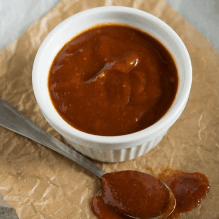 A small glass bowl of reddish-brown Bojangles BBQ sauce served with crispy fried chicken tenders and seasoned fries.