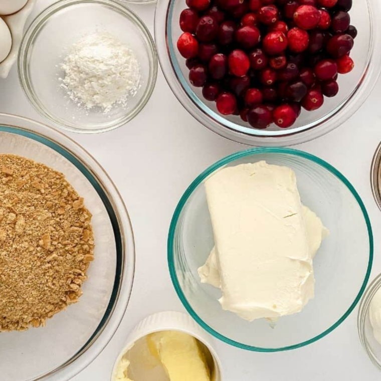 Ingredients for air fryer cranberry bread laid out in bowls: cranberries, flour, sugar, eggs, oil, milk, and an orange