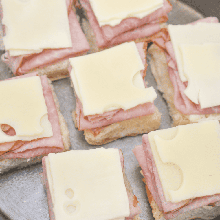 Hawaiian rolls layered with deli ham and Swiss cheese ready to be topped with garlic butter.
