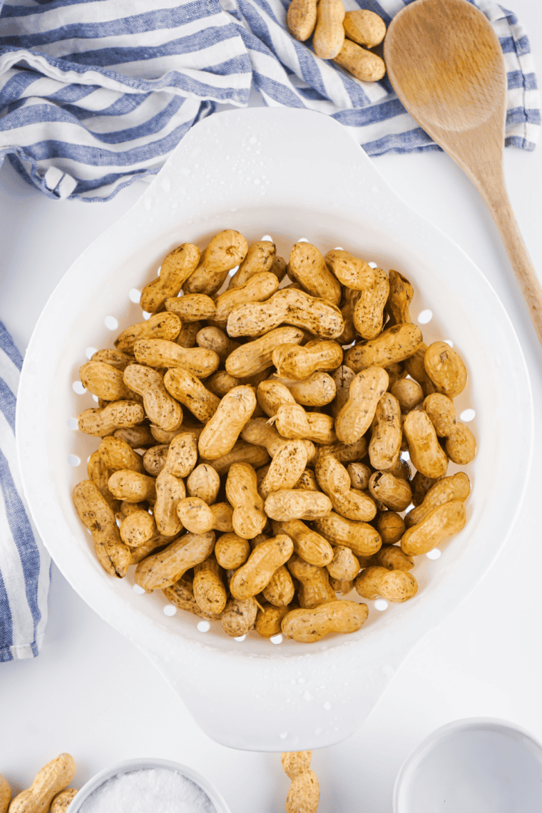 Rinse the Peanuts: Raw peanuts in a colander being rinsed under running water.