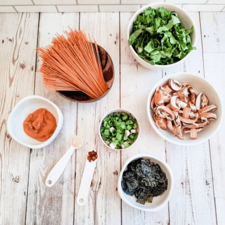 Chopped seaweed squares, thinly sliced baby Bella mushrooms, sliced spring onions, and finely chopped bok choy greens prepared for miso soup.