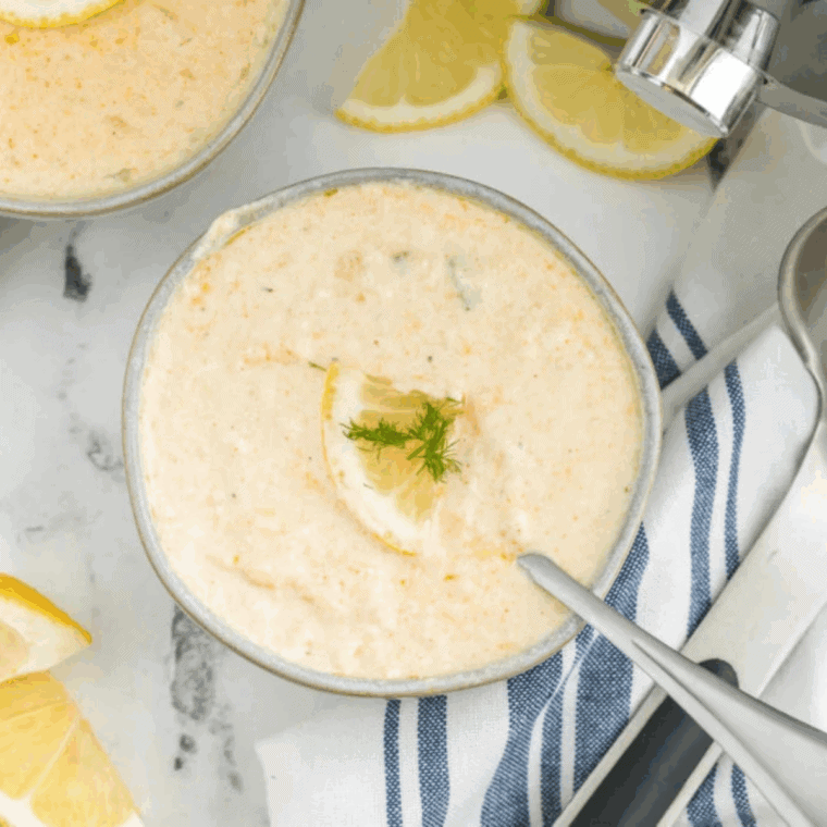 Serving creamy she-crab soup in bowls, topped with fresh herbs