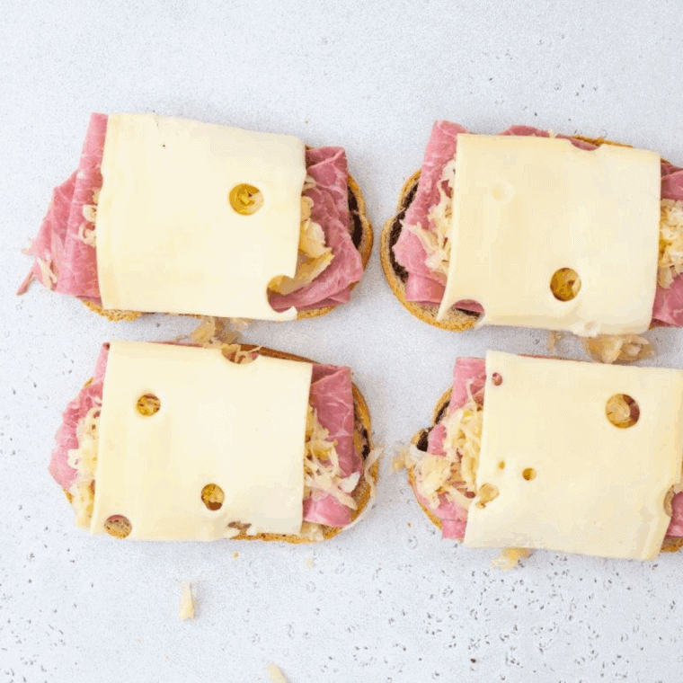 Layering corned beef, sauerkraut, and Swiss cheese on bread for Reuben sandwich.