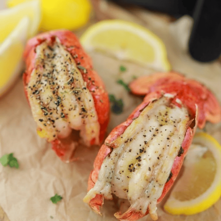Air fryer lobster tails brushed with lemon garlic butter, garnished with parsley and lemon wedges