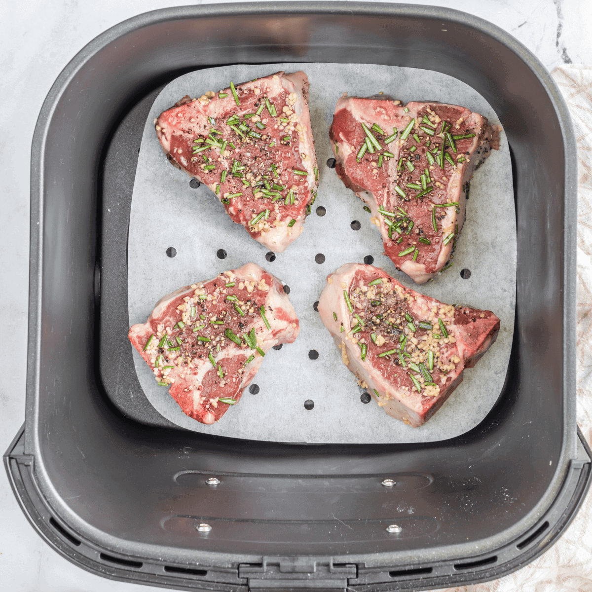 Seasoned lamb chops spaced out in air fryer basket