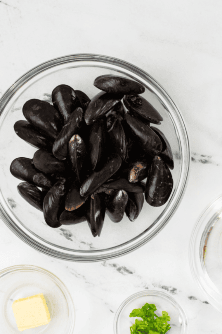 Cleaning fresh mussels under cold water, removing beards and scrubbing shells before cooking.