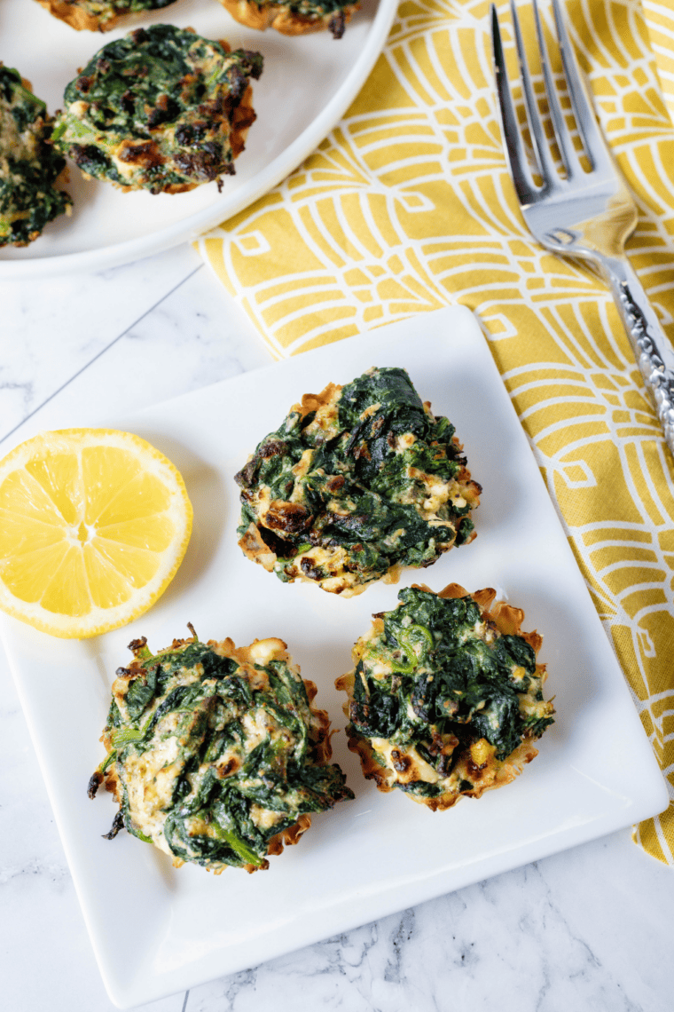 Crispy golden air fryer spanakopita phyllo cups filled with spinach and feta on a serving plate.