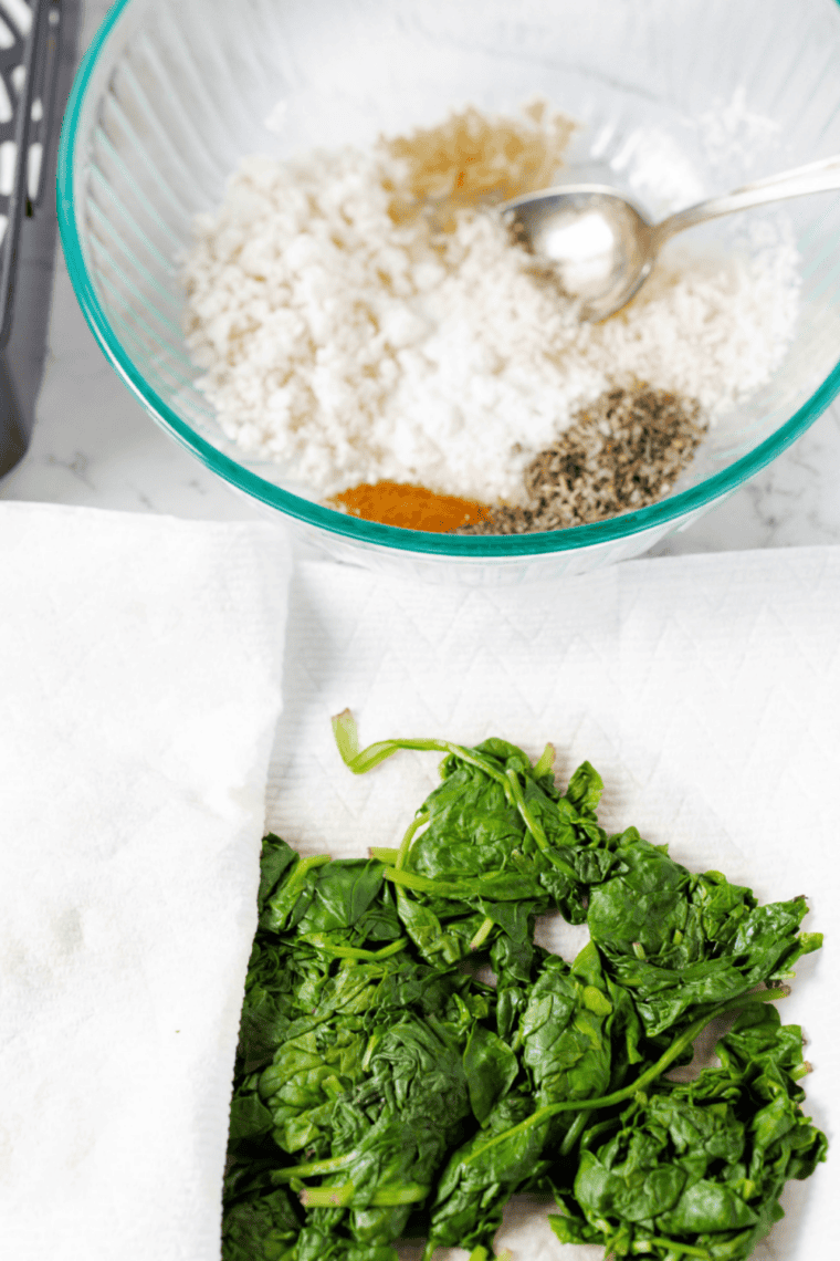 Wilted spinach being pressed in paper towels to remove water.