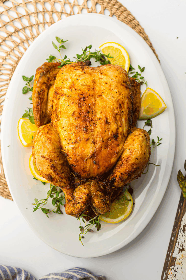Golden-brown roasted Amish whole chicken on a serving platter, garnished with fresh herbs.