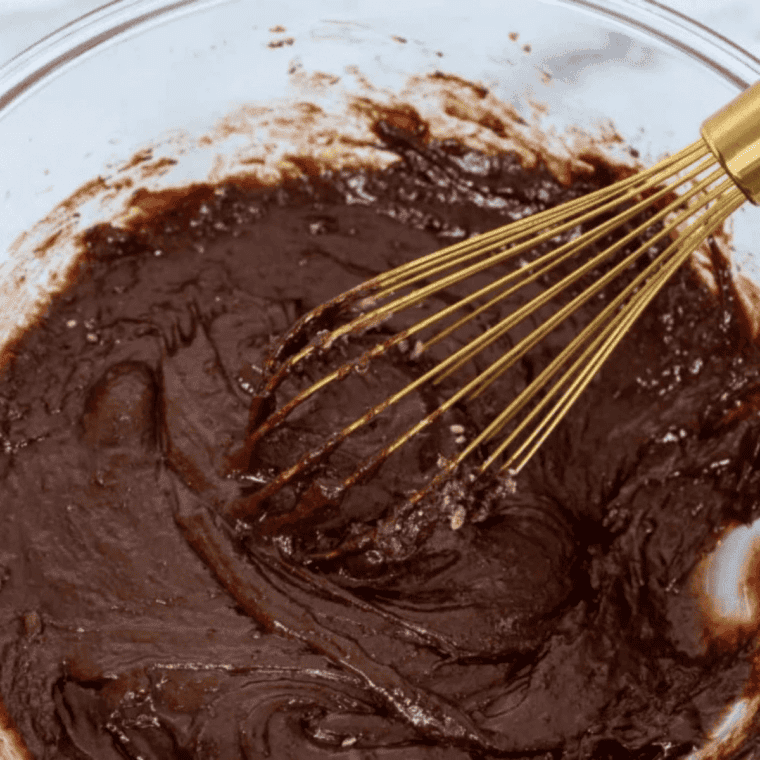 Brownie mix, eggs, oil, and water being stirred into smooth batter in a bowl