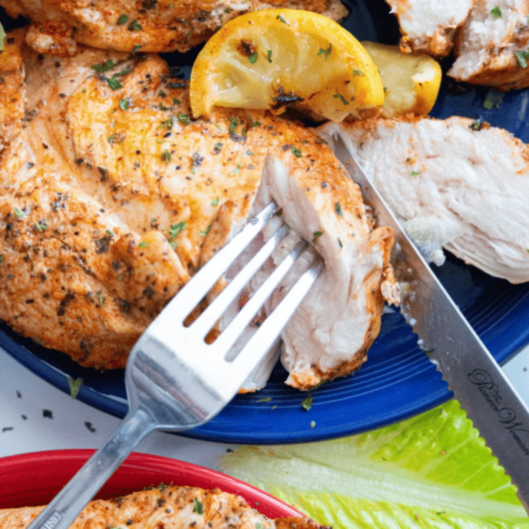 Juicy air fryer lemon pepper chicken breast sliced on a white plate with fresh lemon wedges and parsley