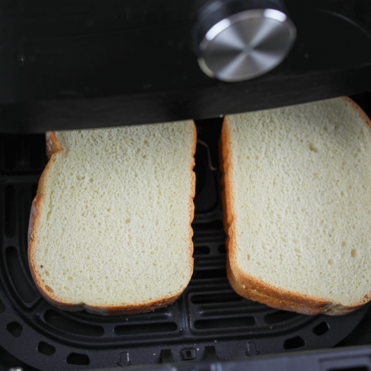 Bread slices toasting in air fryer basket until golden and crisp on the edges