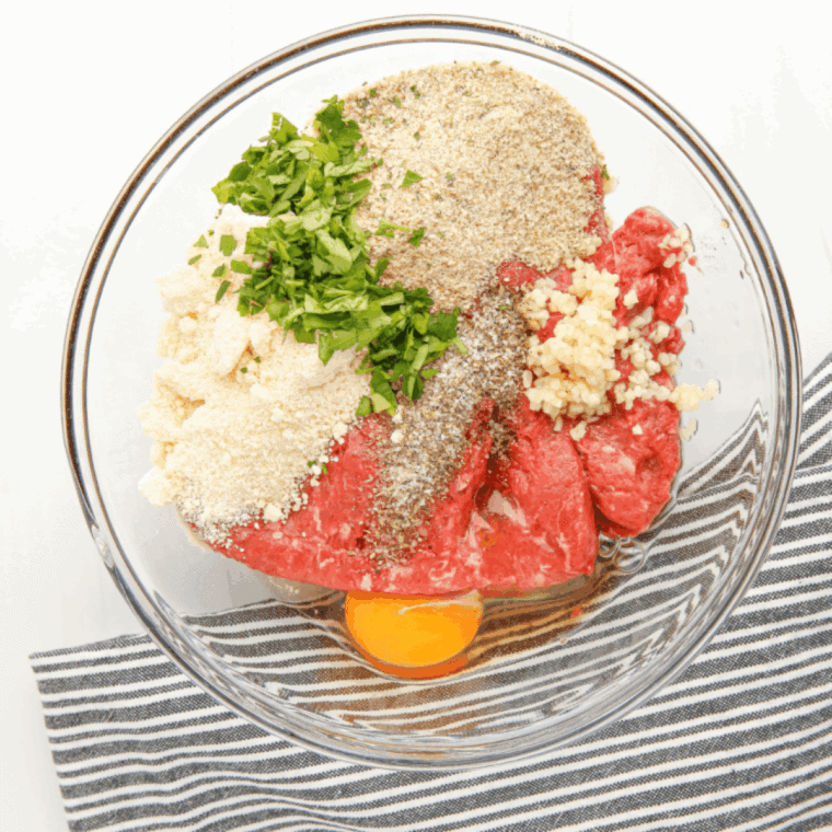 Large bowl with ground beef, Italian sausage, breadcrumbs, eggs, Parmesan, garlic, and seasonings being mixed.