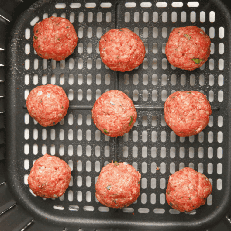 Meatballs arranged in an air fryer basket cooking to golden brown.