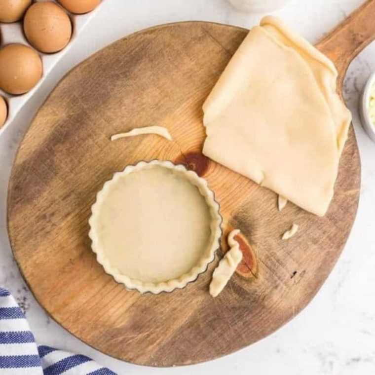 mini tart pan filled with pie crust on round wooden board