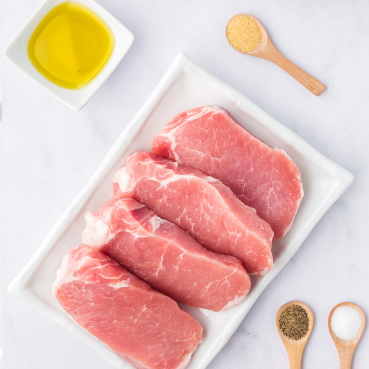 Ingredients for air fryer blackened pork chops: raw pork chops, paprika, garlic powder, onion powder, dried thyme, basil, oregano, cayenne and olive oil in bowls