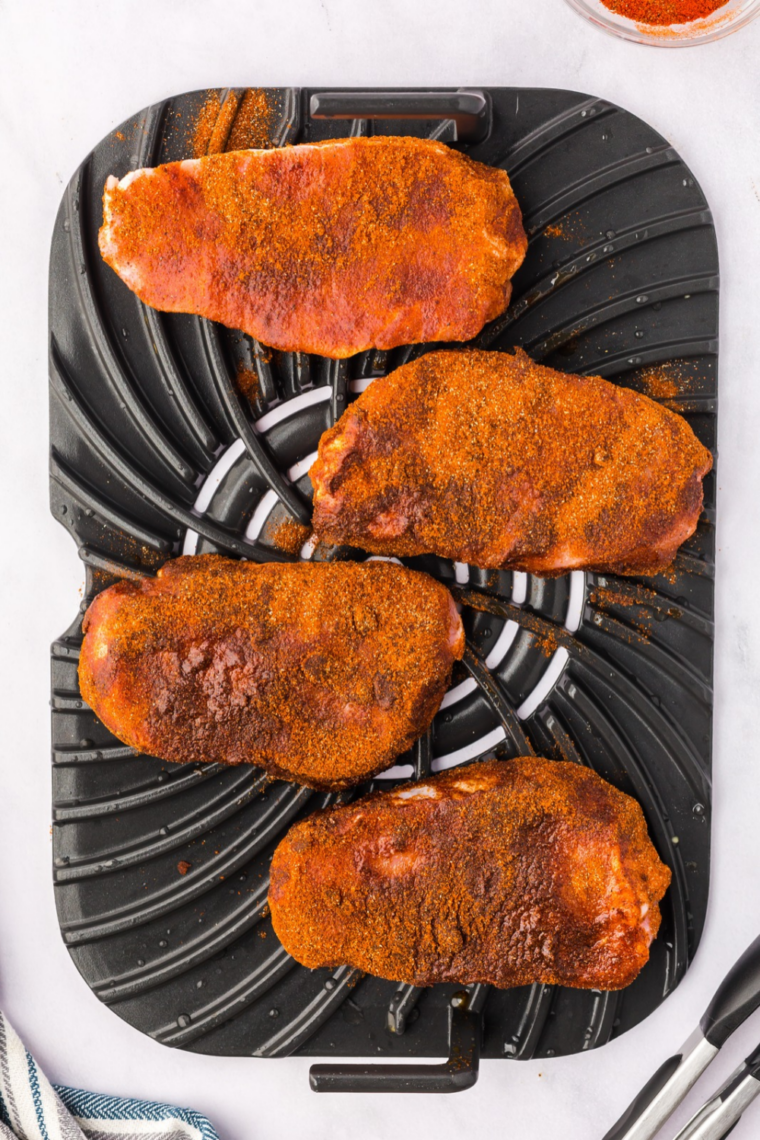 Seasoned pork chops in a single layer in the air fryer basket, flipped halfway to a dark blackened crust