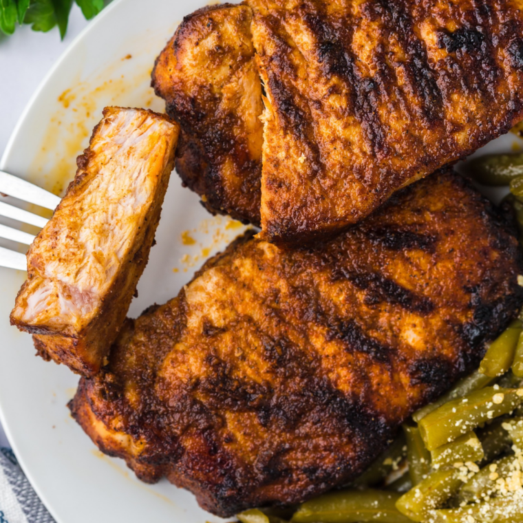 Air fryer blackened pork chops on a white plate with roasted green beans and a lime wedge