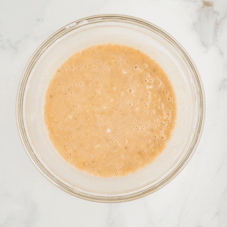 Close-up of mashed ripe bananas in a mixing bowl, slightly chunky for added muffin texture.