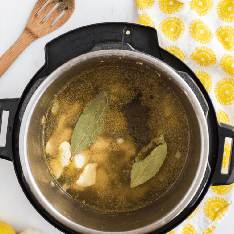 Chicken, rice, broth, and bay leaves added to the Instant Pot before pressure cooking Greek lemon chicken soup