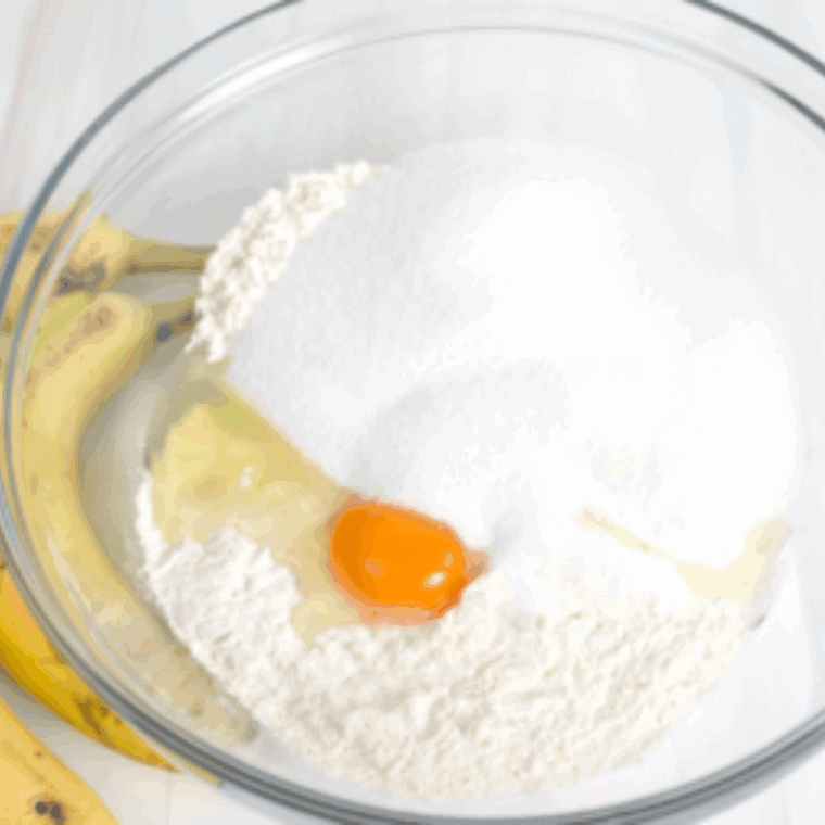 Mixing mashed bananas, butter, sugar, egg, vanilla, baking soda, baking powder, cinnamon, and flour in a large bowl to make banana nut muffin batter