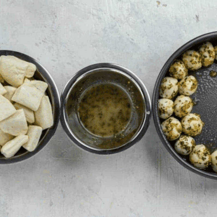 Cutting biscuit dough into pieces, rolling into balls, coating with garlic herb butter, and placing them in a baking pan.