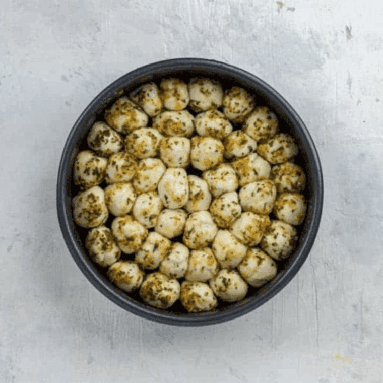 Pan filled with herb and Parmesan coated biscuit dough balls placed into the air fryer basket to cook.