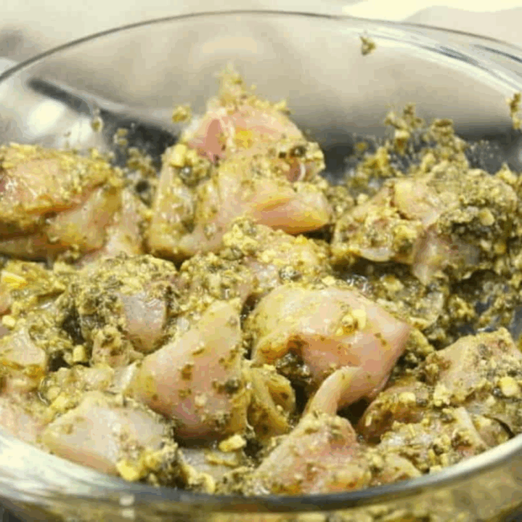 Cubed chicken coated in pesto marinade in a glass bowl, ready to marinate before cooking.
