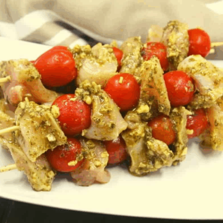 Chicken and cherry tomatoes threaded on skewers in an air fryer basket, cooking at 350°F until golden and tender.