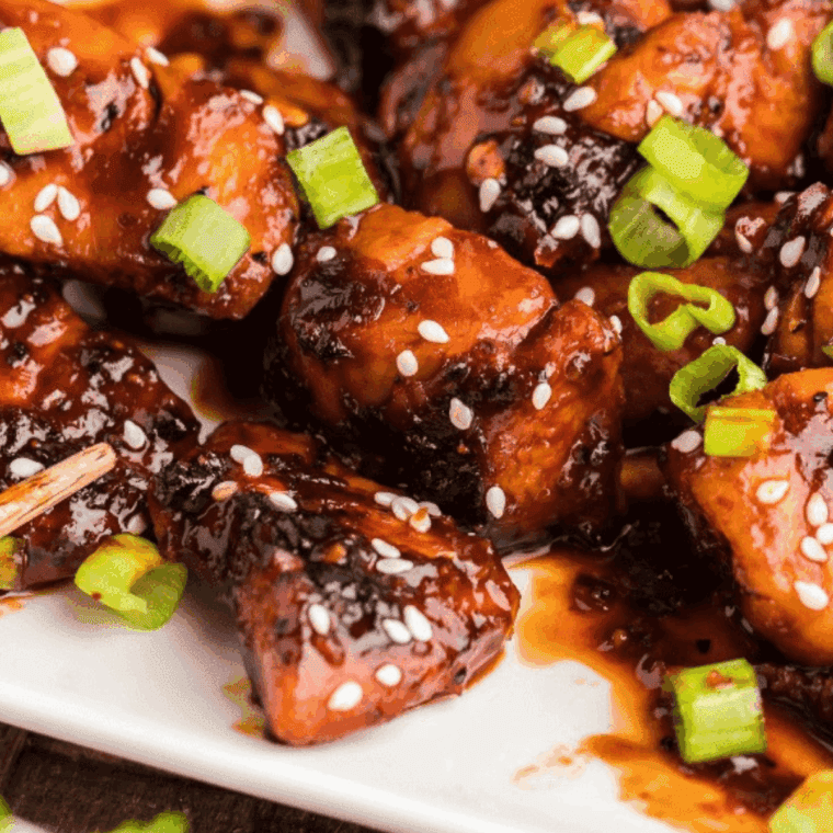 Plated firecracker chicken bites garnished with sesame seeds and green onions.