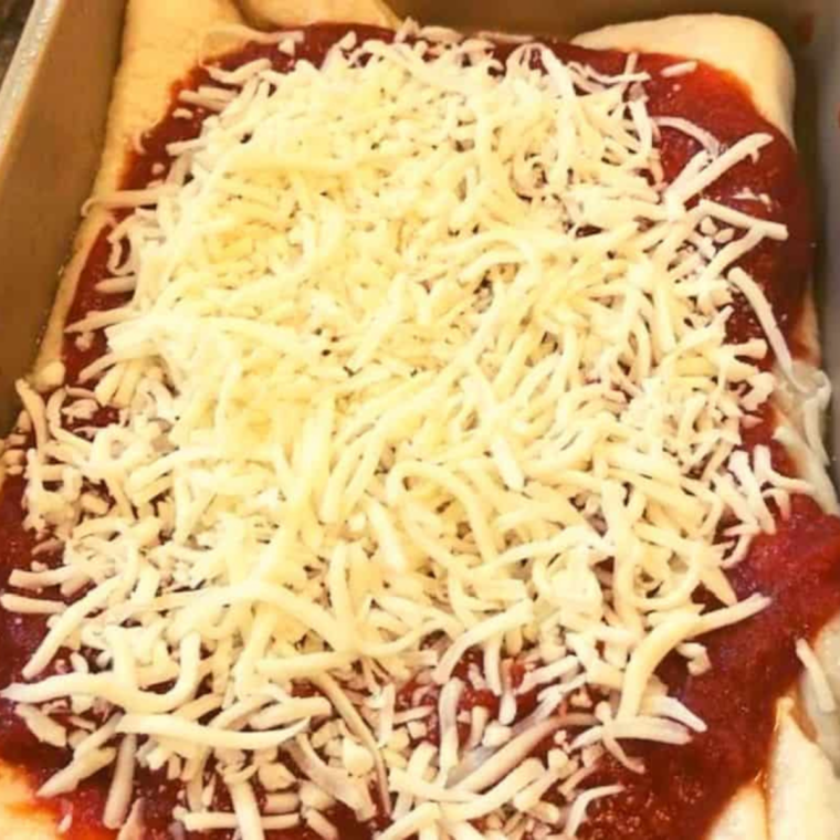 Sliced mozzarella layered directly on raw pizza dough inside the pan before sauce is added.