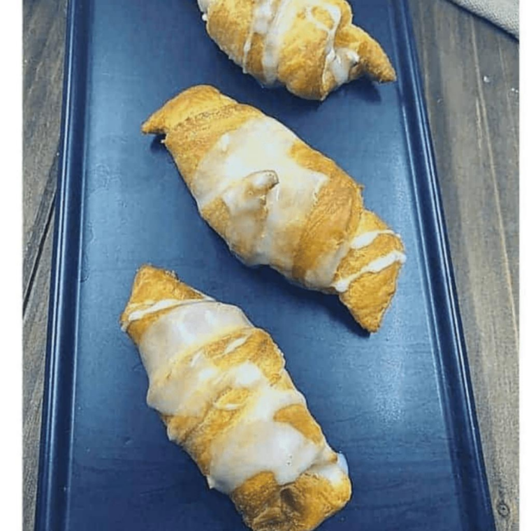 Golden air fryer crescent rolls filled with lemon cheesecake and drizzled with glaze