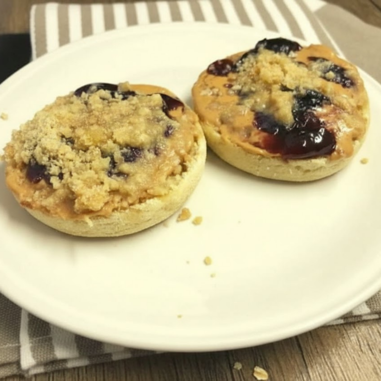 Plate of toasted English muffins topped with peanut butter, jelly, and golden oat streusel crumble from the air fryer.