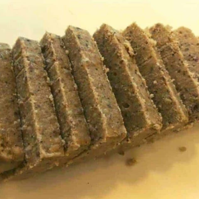 Cold scrapple loaf being sliced into half-inch pieces with a sharp knife