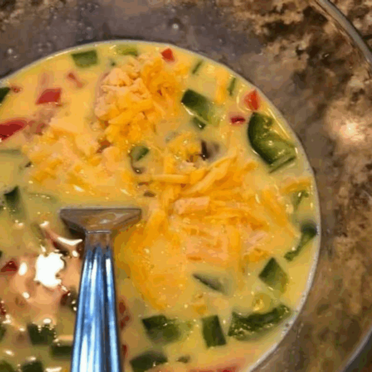 Diced bell peppers and cooked ham mixed with eggs, milk, cheese, salt, and pepper in a bowl.