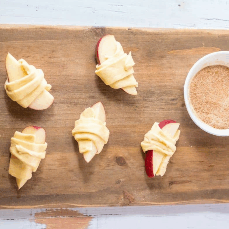 Apple slices placed on halved crescent dough triangles, ready to be rolled.