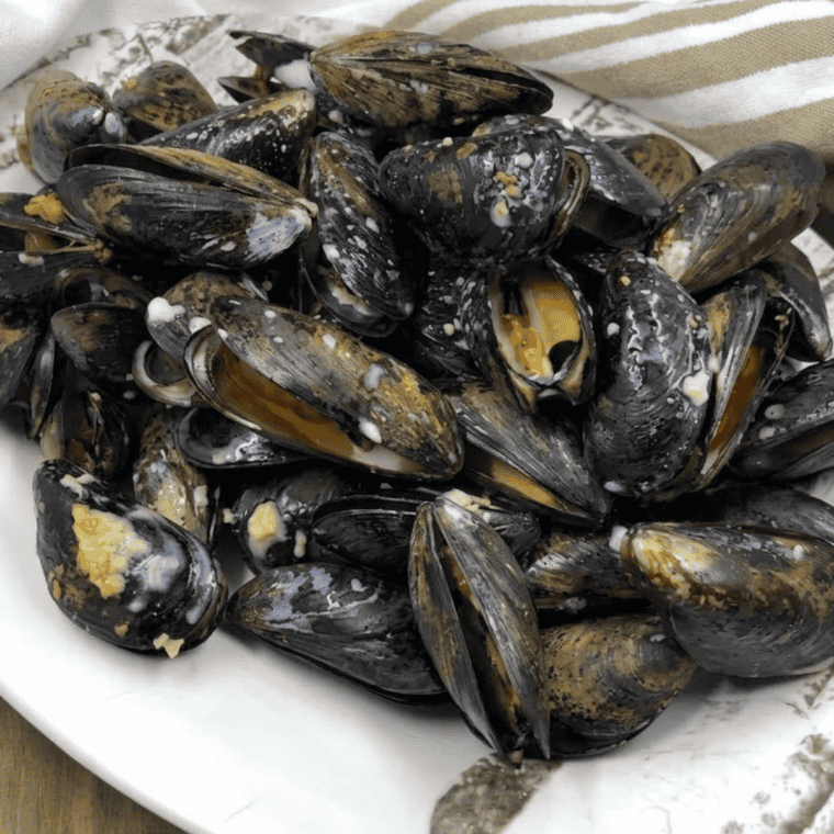 Golden, garlic-butter coated mussels in an air fryer basket, ready to serve.