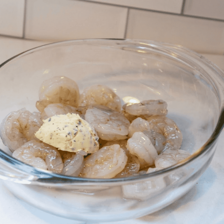 Raw shrimp in a bowl coated with garlic, butter, olive oil, salt, and pepper.