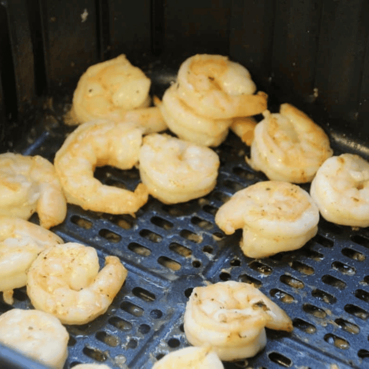Golden cooked shrimp being removed from the air fryer basket.