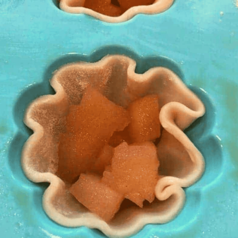 Cinnamon apple filling spooned into crust-lined silicone mold cavities