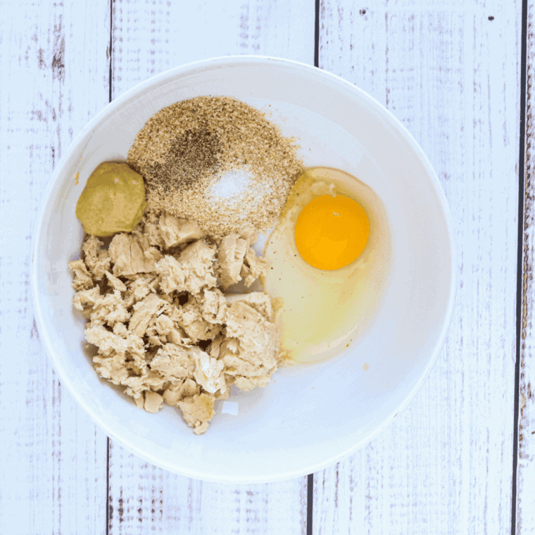combining tuna, eggs, breadcrumbs, chopped vegetables, and seasonings in a mixing bowl for tuna patty mixture