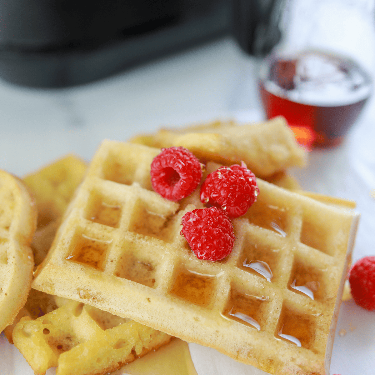 Golden homemade waffles cooked in the air fryer, stacked on a plate with butter and maple syrup.