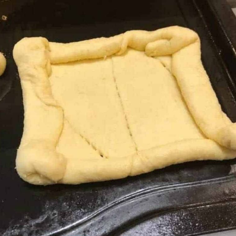 Scored dough with edges pinched up. Alt text: "Crescent dough sheet cut into four squares with raised edges on parchment paper.