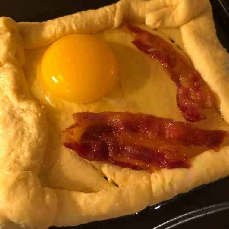 Squares filled with eggs and bacon, pre-air-fryer. Alt text: "Four crescent dough squares filled with raw eggs and cooked bacon, ready to be air fried.