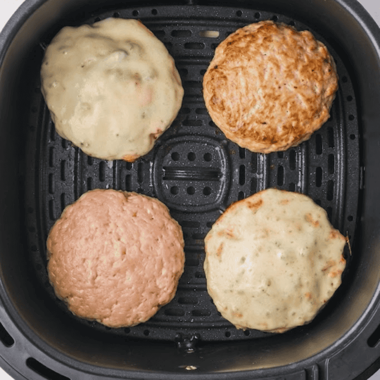 Golden, juicy cooked Greek chicken burgers in the air fryer basket after flipping