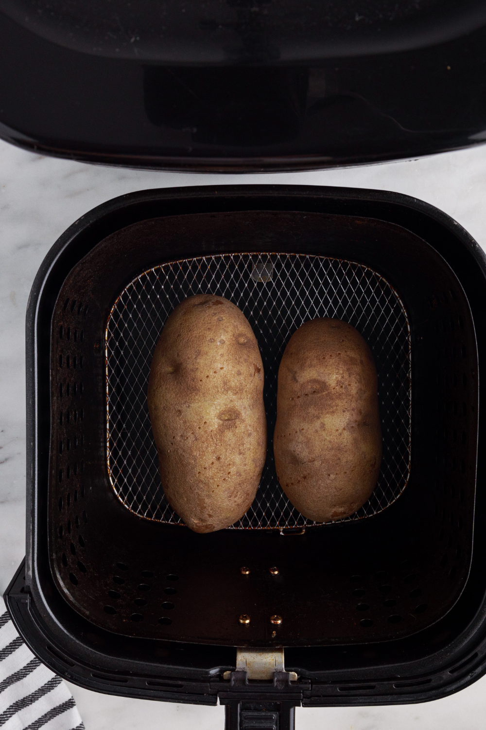 Air fryer baked potatoes cooking at 400&deg;F with flipping halfway through until fork tender and fully cooked inside.