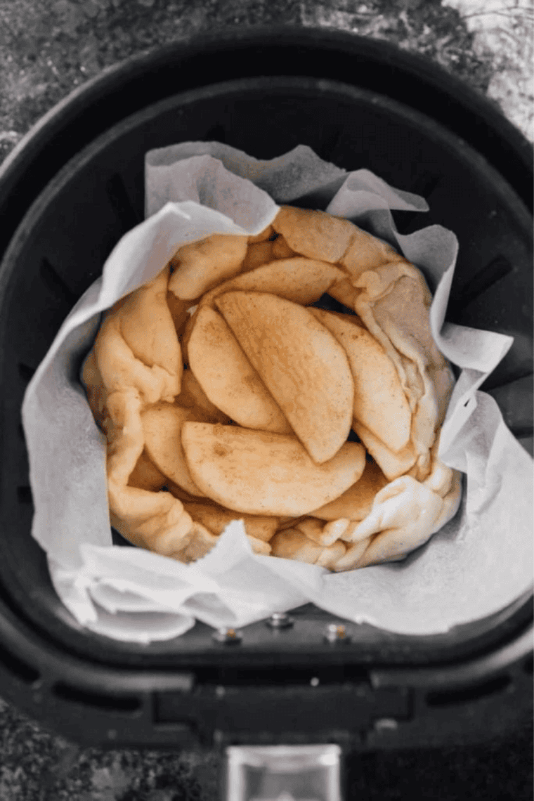 Assembled apple galette on parchment in the air fryer basket before cooking