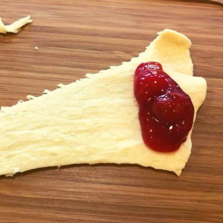 Cherry pie filling spooned onto the wide end of crescent roll dough triangles with optional cream cheese base for filling before rolling pastry dessert