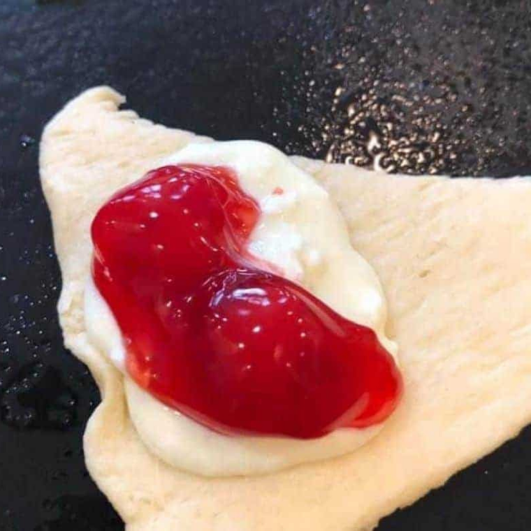 Crescent dough being filled with cream cheese and cherry pie filling, ready to roll.